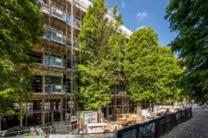 Een appartementencomplex aan de Karel du Jardinstraat is in renovatie, omringd door steigers en grote bomen.